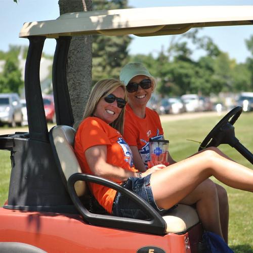 two women sitting in a golf cart next to eachother