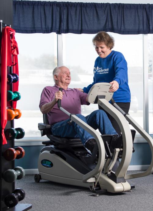 An older man using an exercise machine while his physical therapist supervises him