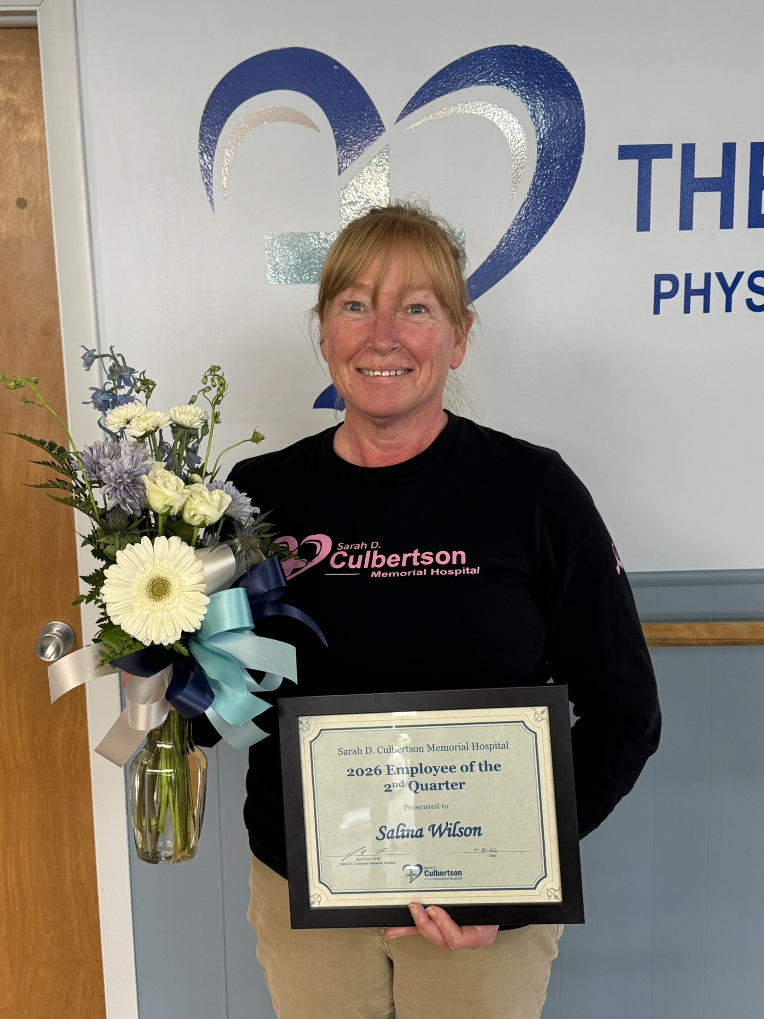 Red haired woman holding flowers and an employee of the quarter certificate